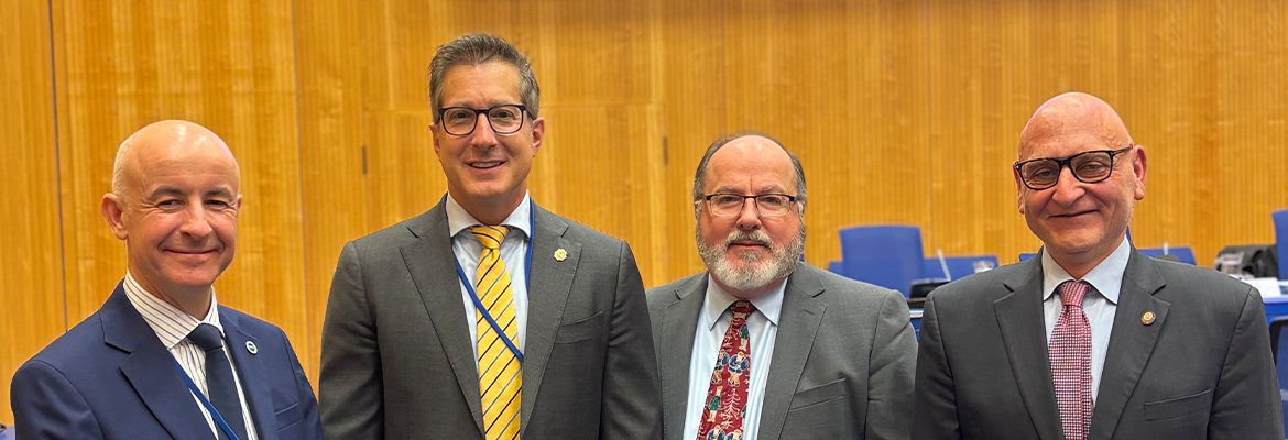 Image of four men standing in a large room smiling at the camera. 
