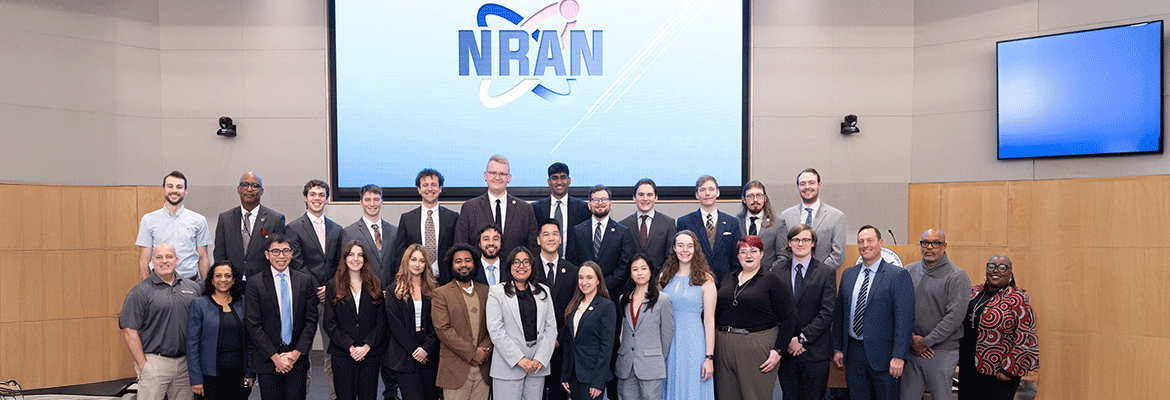 A large group of professionally dressed adults pose for a group photo in an auditorium.